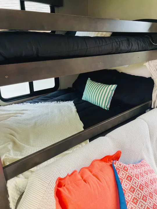 An inviting RV rental interior with comfortable bunk beds, complete with black bedding, soft blankets & decorative pillows.. Grand Design 265BH 2023