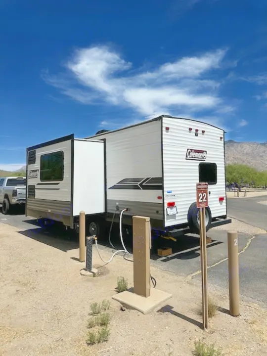 White & grey travel trailer RV rental parked at a sunny campsite with hookups. Site 22, ready for your next adventure.. Dutchmen Coleman Lantern 2022