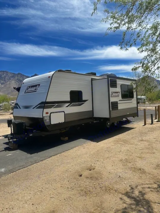 White and grey Coleman travel trailer set up at a sunny mountain RV campsite; ideal for an rv rental getaway.. Dutchmen Coleman Lantern 2022