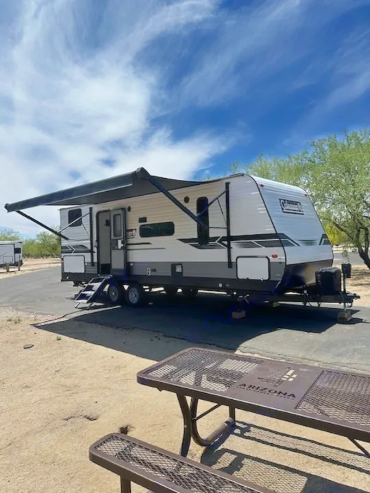 An RV rental, a white travel trailer, is set up at an Arizona State Park campsite with an extended awning and picnic table.. Dutchmen Coleman Lantern 2022