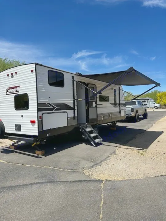 This RV rental is parked and set up with an extended awning under a clear, sunny sky, ready for a desert adventure.. Dutchmen Coleman Lantern 2022