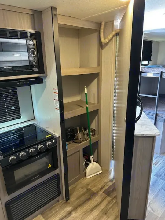 Inside an RV rental: compact kitchen with microwave, stove, oven, and ample storage shelves. Perfect for travel!. Dutchmen Coleman Lantern 2022