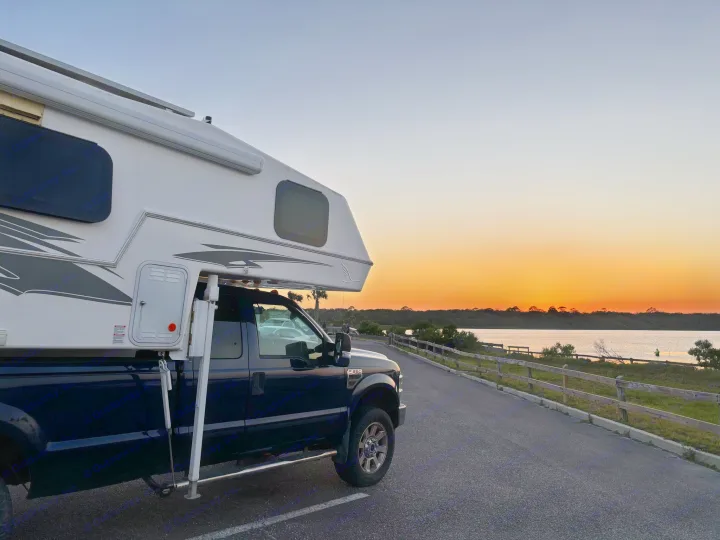 Truck camper parked by water at sunset. Imagine this view with your RV rental adventures!. Northern Lite 9-6 Wet Bath 2022