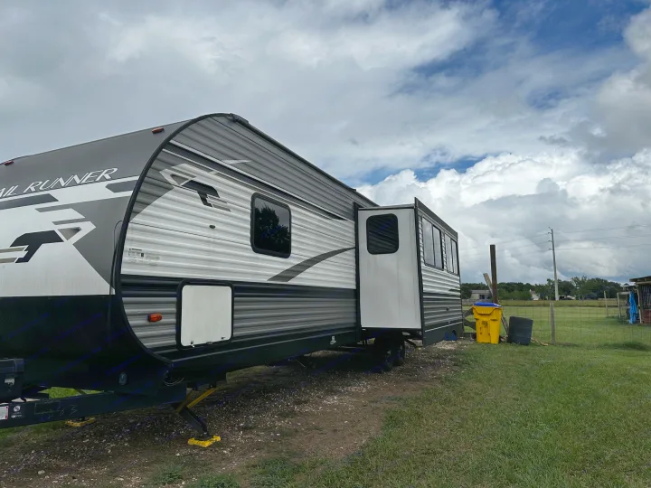 A gray Trail Runner RV rental, a travel trailer with a slide-out, parked on gravel under a cloudy sky, ready for camping.. 5sfeb3729me459252 31DB 2021