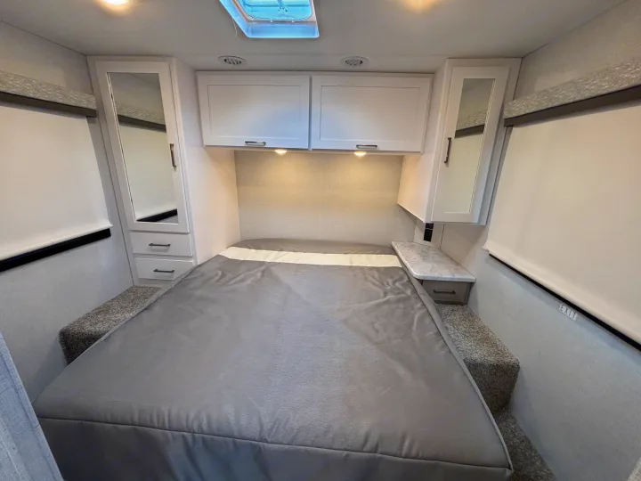 A bright and cozy rv rental bedroom with a gray bed, overhead cabinets, mirrored wardrobes, nightstands, and a skylight.. Thor Motor Coach Four Winds 2026