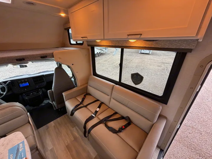Spacious RV rental interior featuring a cockpit, over-cab bed, sofa with seatbelts, and overhead cabinets for comfortable travel.. Thor Motor Coach Four Winds 2026