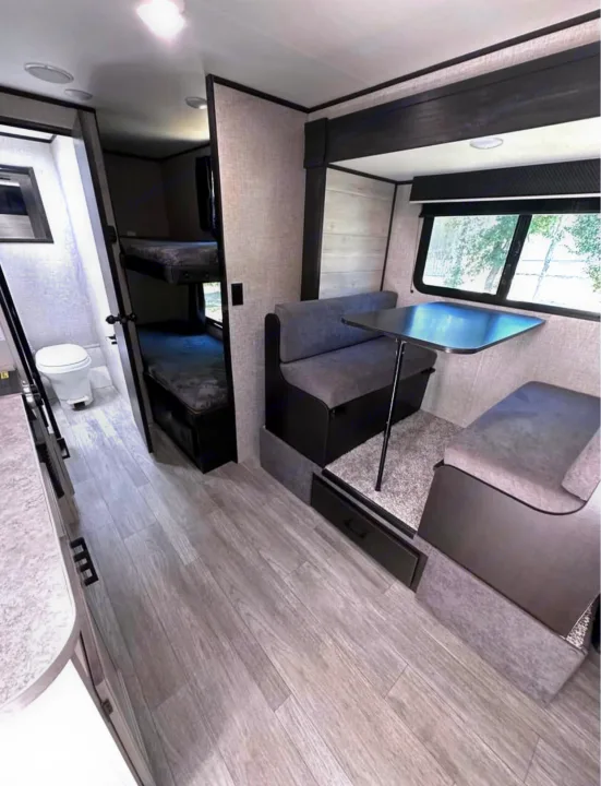 RV rental interior: light wood-look floor leads past bathroom & bunks to modern dinette. Practical, compact living.. Jayco Jay Flight SLX 2022