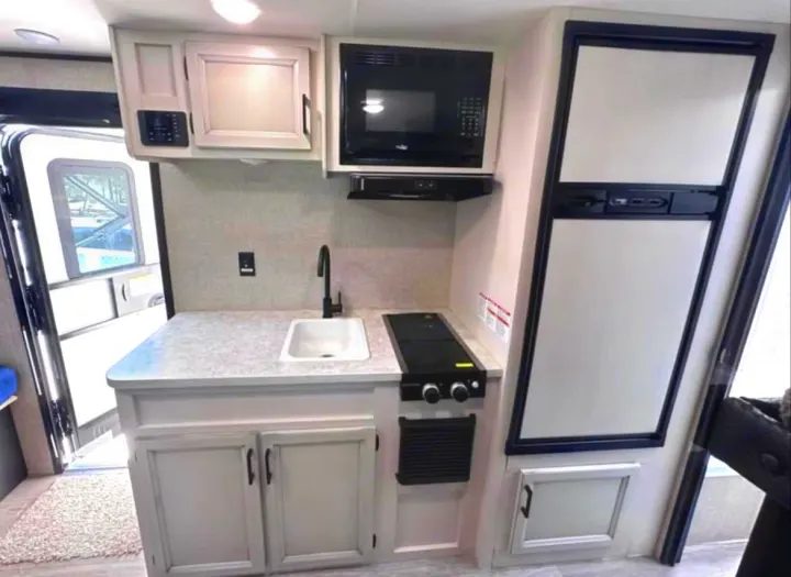 A compact rv rental kitchen featuring light cabinets, sink, microwave, stovetop, and refrigerator, ideal for travel.. Jayco Jay Flight SLX 2022