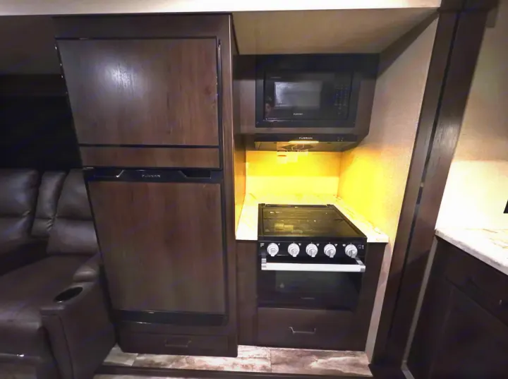 Well-equipped RV rental kitchen with Furrion fridge, microwave, and stove, plus nearby cozy couch seating.. Grand Design Transcend Xplor 2022