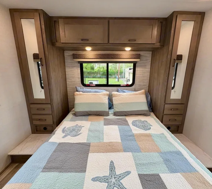 Experience comfort in this RV rental's cozy bedroom, featuring a nautical quilt, mirrored side cabinets, and a window view.. Gulf Stream Conquest 2025
