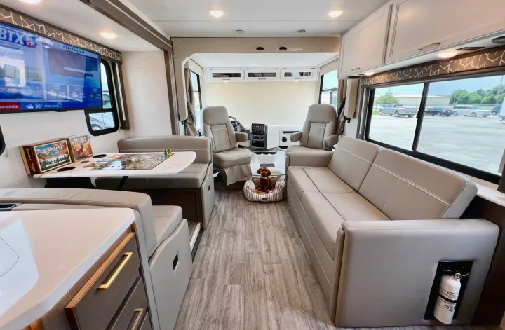This **rv rental** interior offers a comfy living area with a dining booth, sofa, TV, board games, and a dog bed for your travel trip.. Thor Motor Coach A.C.E 2024