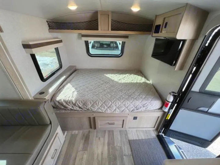Step inside this RV rental! Features include a cozy bed, wall-mounted TV, overhead storage, and a small couch.. Rockwood GeoPro 2022