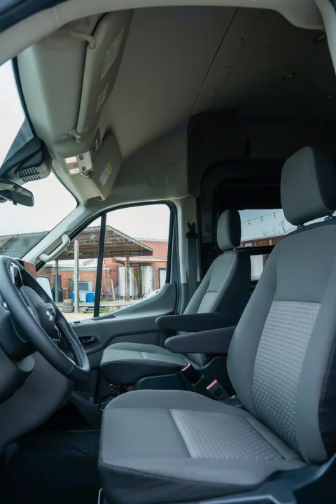 Inside an RV rental van. View from rear shows driver's cabin, comfy front seats, & outdoor scene through windshield.. Ford Transit Custom 2022