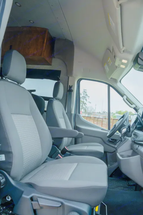 Inside an RV rental, highlighting the spacious front cabin with comfy gray seats, dashboard, and custom overhead cabinetry.. Ford Transit Custom 2022