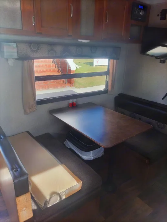 Bright RV rental interior: dinette with window, wood table, and upholstered bench seating. Ideal for travel dining.. Keystone RV Springdale Eco-Lite 2018