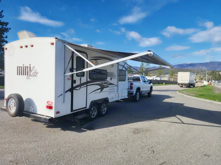A white Mini Lite travel trailer RV rental, with its awning open, is hitched to a pickup truck, parked outdoors.. Forest River Rockwood Mini Lite 2014