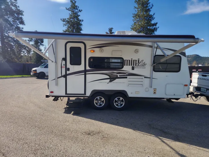 White Mini Lite travel trailer, a perfect RV rental, with awning extended, parked on asphalt.. Forest River Rockwood Mini Lite 2014