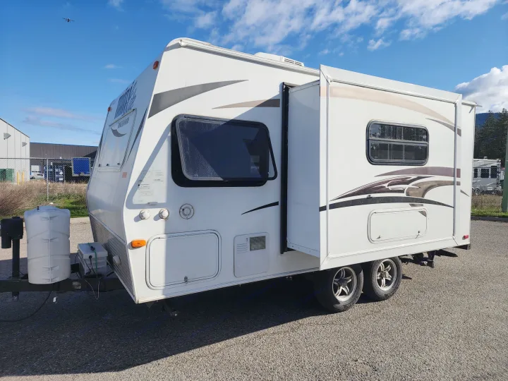 White travel trailer RV rental, featuring an extended slide-out, parked on asphalt under a bright blue sky.. Forest River Rockwood Mini Lite 2014