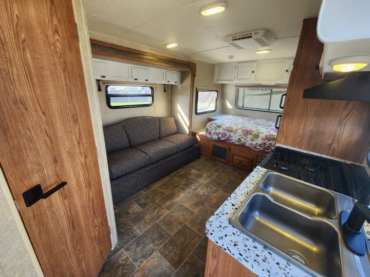 Spacious RV rental interior featuring a living area with sofa, bedroom with a floral bed, and a full kitchen.. Forest River Rockwood Mini Lite 2014