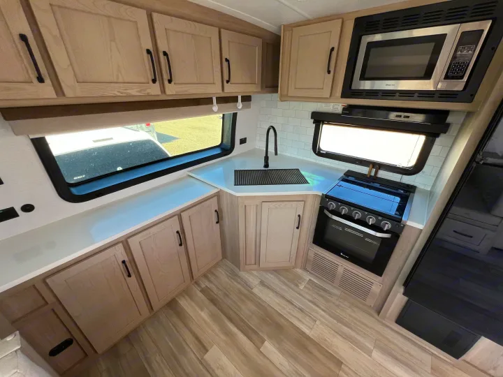 Modern kitchen in an RV rental, showcasing light wood cabinets, subway tile, a sink, oven, and microwave for cooking.. Forest River Rockwood Ultra Lite 2024