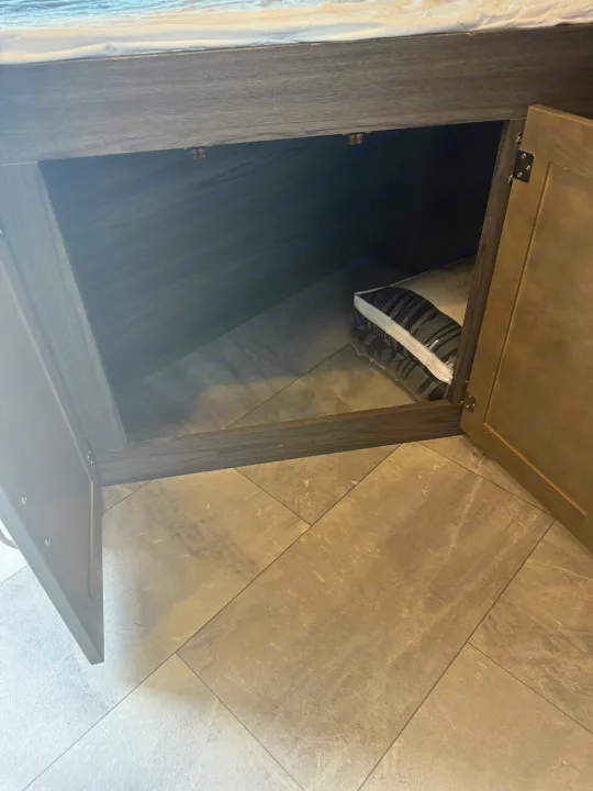 Inside an RV rental's clever under-bed storage, a new, striped bedding set sits on the light gray tiled floor.. Dutchmen Kodiak Ultra Lite 2021