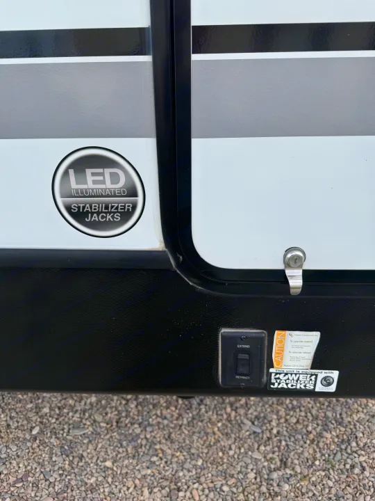RV rental close-up: Power stabilizer jacks with LED illumination and operating controls on the side panel.. Dutchmen Kodiak Ultra Lite 2021