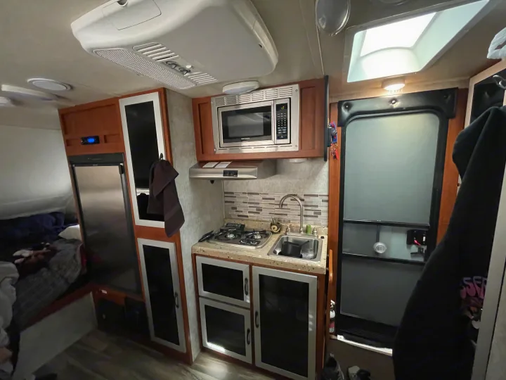 Cozy RV rental interior: Kitchenette with stove, sink, microwave, fridge, and a nearby sleeping area for travelers.. Travel Lite Falcon 2018