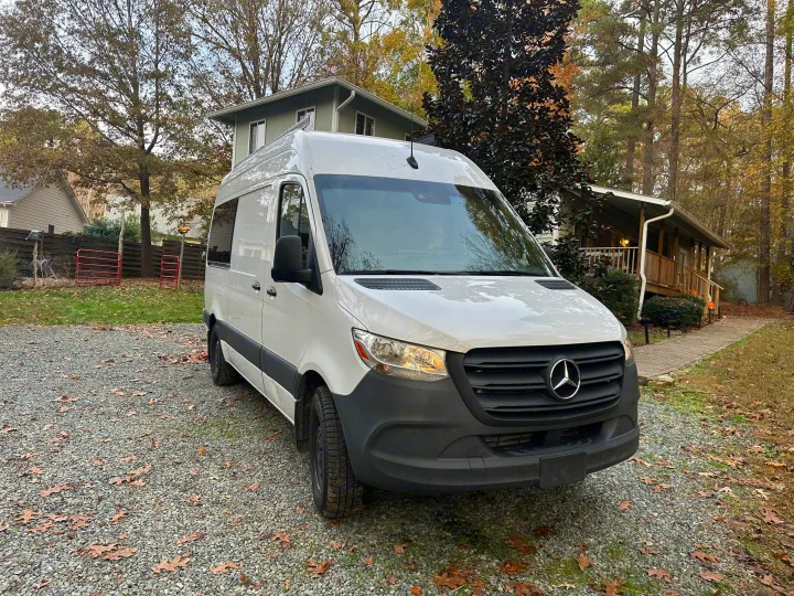 White Mercedes-Benz Sprinter van, ready for RV rental, parked on a gravel driveway with homes & trees.. Mercedes-Benz Sprinter 2020