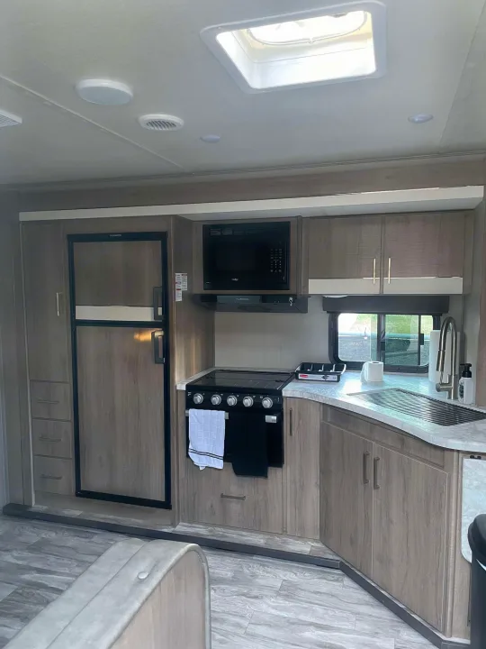 Inside this RV rental: modern kitchen with a fridge, microwave, stove, sink, and storage cabinets.. Grand Design Imagine XLS 2022