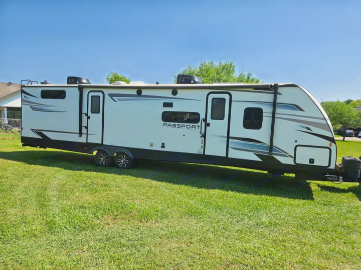 An RV rental option: a sleek white Keystone Passport travel trailer, parked on a sunny green lawn under clear skies.. Keystone RV Passport GT 2022