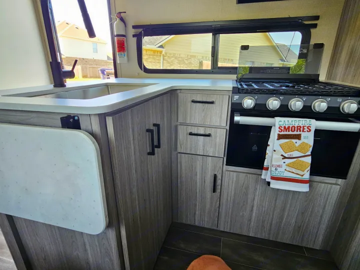 This RV rental kitchen combines functionality and style with a compact sink, stove, cabinets, and an extendable counter.. Keystone RV Passport GT 2022