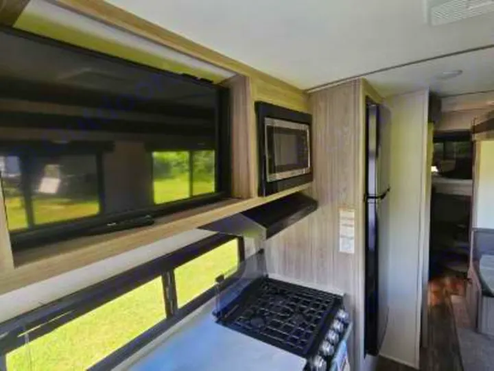 This RV rental interior features a kitchen with a stove, microwave, refrigerator, and a TV in the living area.. Keystone RV Passport GT 2022