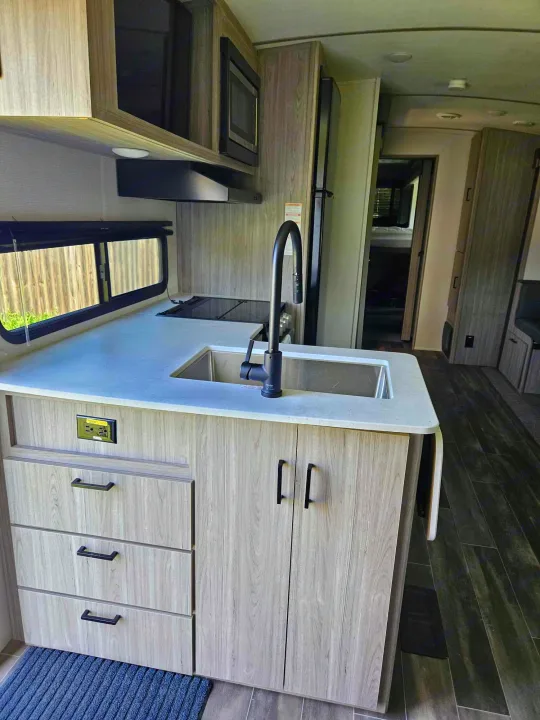RV rental kitchen featuring a modern sink, cooktop, microwave, & ample counter space.. Keystone RV Passport GT 2022