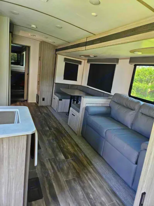 Spacious RV rental interior: modern living area with a grey sofa, U-shaped dinette, and wood-look flooring.. Keystone RV Passport GT 2022
