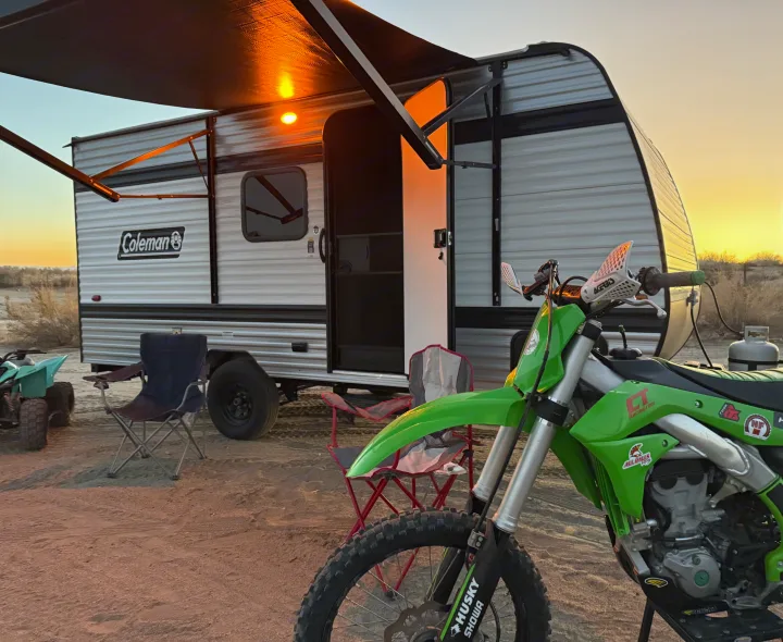 RV rental camping in the desert. A Coleman travel trailer at sunset with a green dirt bike and chairs.. Keystone Coleman 17B 2025