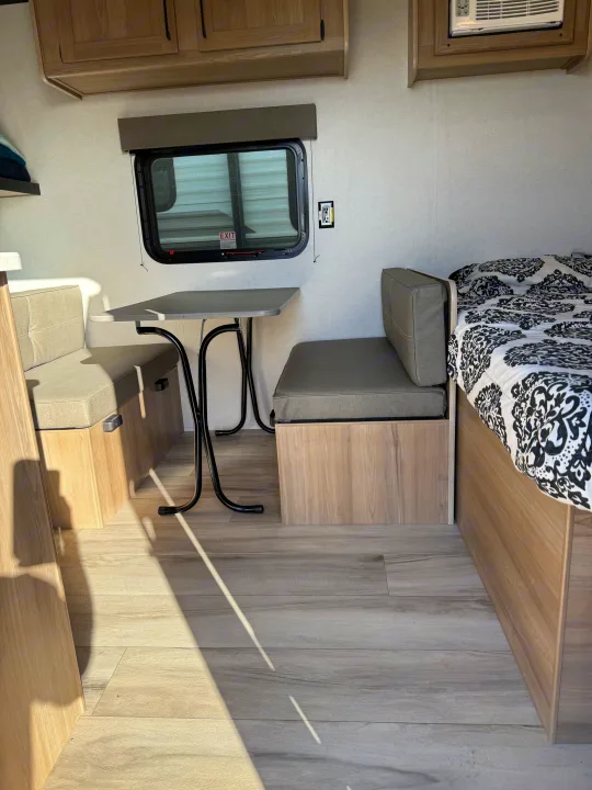 Cozy rv rental interior showcasing a modern dinette, window, overhead storage, and bed with patterned bedding.. Keystone Coleman 17B 2025