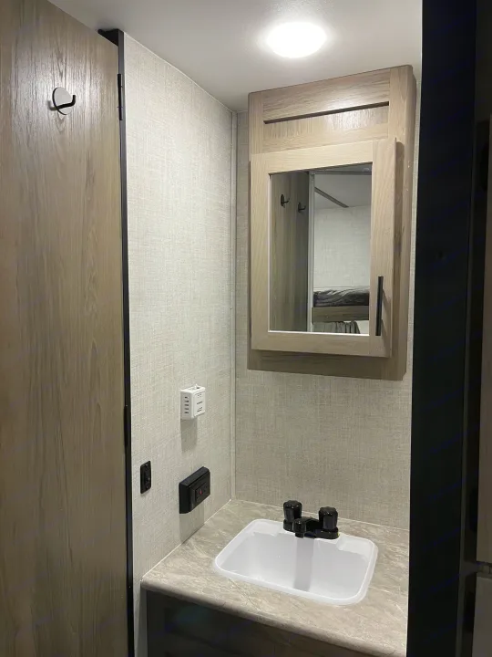 Compact RV rental bathroom with sink, mirror, and door. Features a Dometic thermostat & bunk bed reflection.. Gulf Stream Conquest 2022