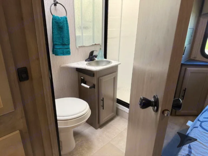 Compact RV rental bathroom features a toilet, sink, mirror, and shower, showcasing functional design for travel convenience.. Coachmen RV Freelander 26DS 2023