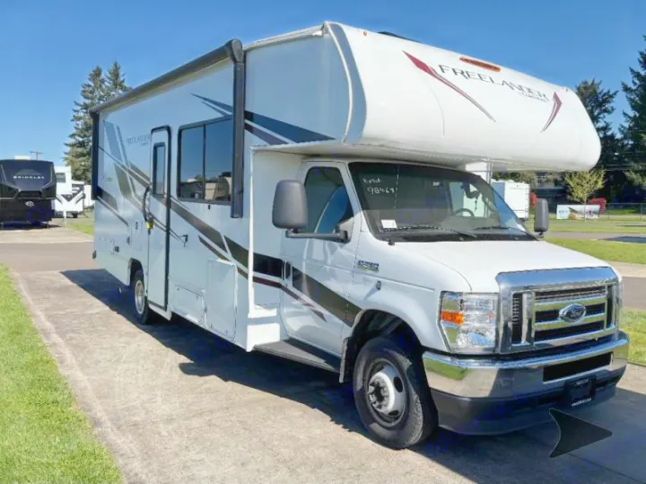 White Class C rv rental with dark stripes, parked on a paved lot. A spacious motorhome for trips.. Coachmen RV Freelander 26DS 2023