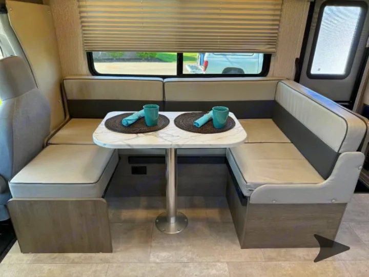 Explore this RV rental's inviting dinette, featuring U-shaped seating, a marble-look table with cups, and window blinds.. Coachmen RV Freelander 26DS 2023