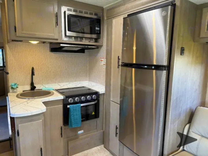 Modern RV rental kitchen featuring light wood cabinets, stainless steel appliances, sink, and stove/oven.. Coachmen RV Freelander 26DS 2023