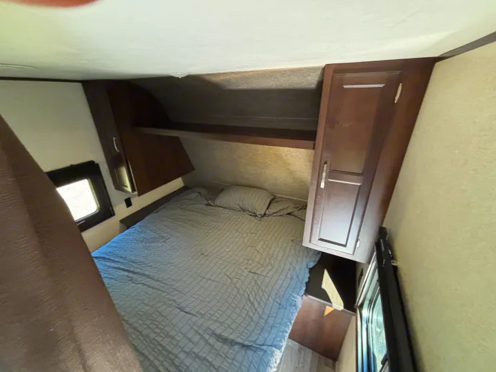 Cozy RV rental bedroom featuring a comfortable bed with overhead storage and windows. Ideal for compact travel.. Jayco Jay Flight 2020