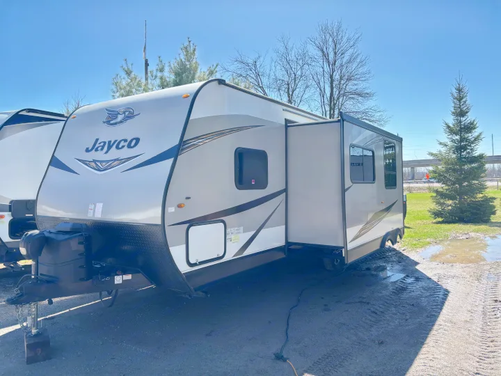Spacious Jayco travel trailer for rv rental, with an extended slide-out, parked on a sunny lot next to muddy puddles.. Jayco Jay Flight 2020