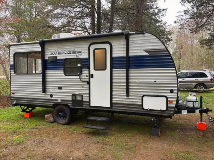 Experience the outdoors! An Avenger LT travel trailer RV rental is leveled in a green campground.. Avenger 16RD 2024