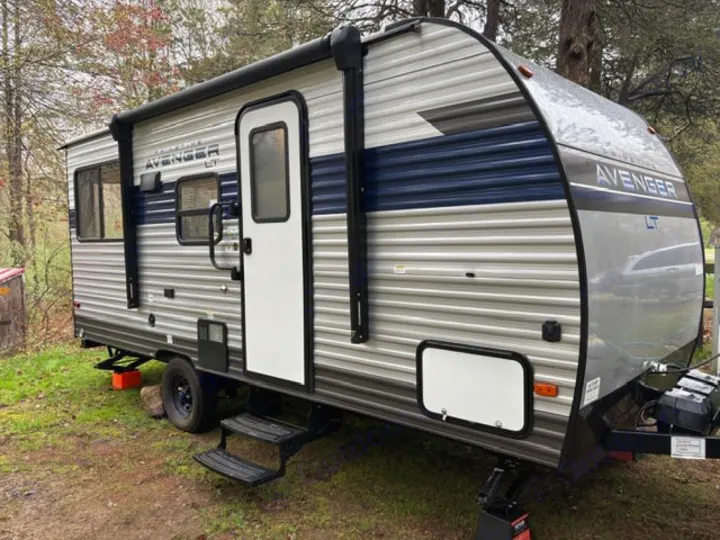 A grey & blue AVENGER LT travel trailer parked at a green campsite, ideal for your next rv rental adventure.. Avenger 16RD 2024