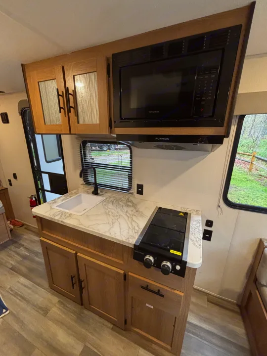 This RV rental's modern kitchen setup: microwave, stovetop, sink, and wood cabinets. Ready for your adventures!. Avenger 16RD 2024