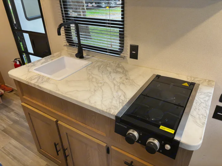 RV rental kitchen: modern sink, black stovetop, and white marble-look countertop over wood cabinets. Clean and functional space.. Avenger 16RD 2024