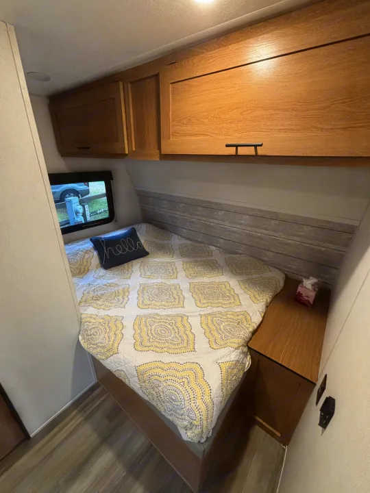 This RV rental bedroom offers a patterned bed, light wood cabinets, and a window, creating a cozy and compact living space.. Avenger 16RD 2024