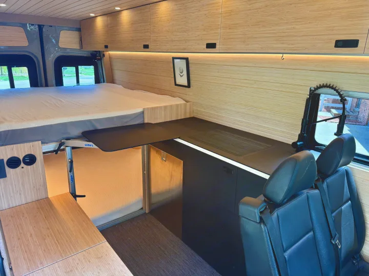 This RV rental interior showcases a raised bed, modern kitchenette with counter, flexible dining table, and passenger seating.. Mercedes-Benz Sprinter 2024