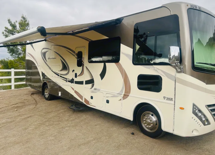 A large beige and brown Thor Hurricane RV rental with its side awning extended, parked on a dirt lot.. Thor Hurricane 2018